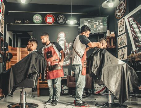 A bustling barbershop with two men getting haircuts, showcasing a vibrant barber environment.