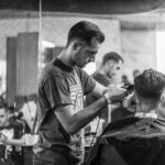 A barber skillfully gives a haircut in a stylish Wrocław barbershop, captured in moody monochrome. U ACADEMY
