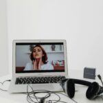 A woman conducting a online video consultation for beauty garage visible on a laptop screen with headphones nearby.