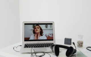 A woman conducting a online video consultation for beauty garage visible on a laptop screen with headphones nearby.