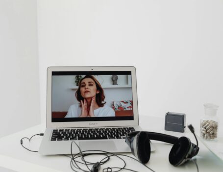 A woman conducting a online video consultation for beauty garage visible on a laptop screen with headphones nearby.