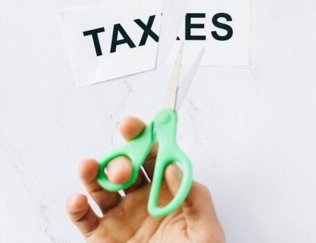 Top-down view of a hand holding scissors cutting the word 'taxes' on a marble surface. GST on Salon Serices has been cut down from 18% to 5%